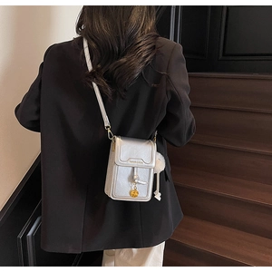 Detail of silver crossbody phone bag with knot decor, golden charm and white fur ball