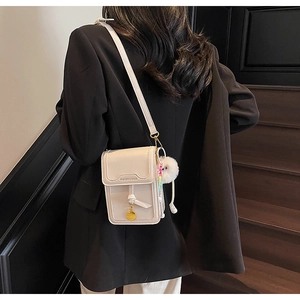Detail of cream crossbody phone bag with litchi texture and cute plush ball charm