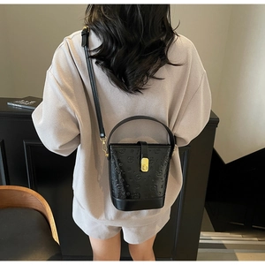 Detail of black bucket bag with bear embossing and gold lock on a model outfit