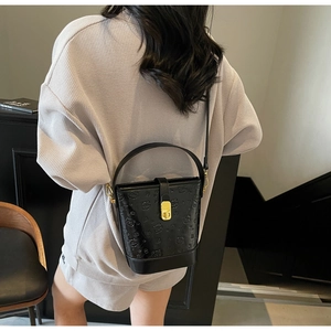 Detail of black bucket bag with bear embossing, gold lock and crossbody strap on model