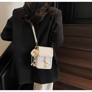 Minimalist crossbody phone bag with plush charm shown on model in a stylish setting