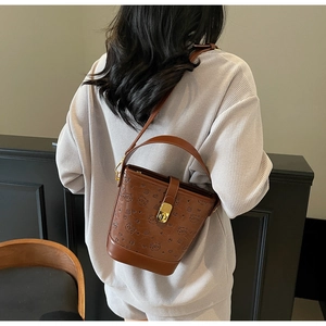 Detail view of brown leather bucket bag with embossed bear pattern and gold metal clasp