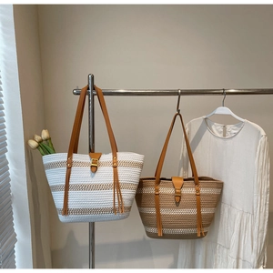 Side view of woven cotton tote bags with leather straps and fringe details on a rack