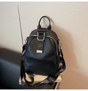 Detail of black pebbled leather backpack with silver hardware on a leather surface