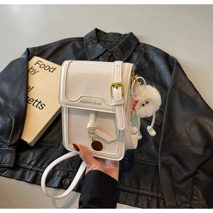 Detail of off-white crossbody bag with gold text and plush charm on leather jacket