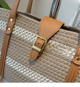 Detail of woven straw tote bag featuring brown leather straps and gold metal buckles