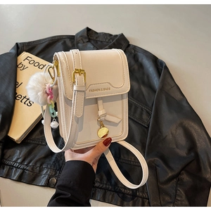 Detail of a beige vertical mini crossbody bag with golden buckle and plush ball charm
