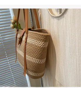 Macro detail of hand-woven straw tote bag with brown leather strap and tassel accents