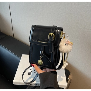 Detail of black glossy PU leather square bag with gold lettering and white plush keychain