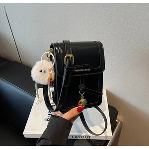 Detail of glossy black crossbody phone bag with gold lettering and white plush charm