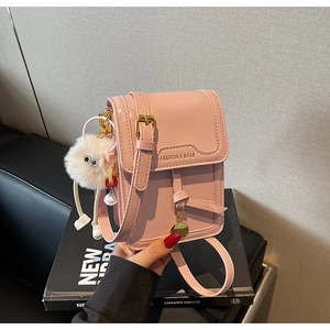 Close-up of pink leather crossbody bag featuring gold hardware and a fluffy pompom charm