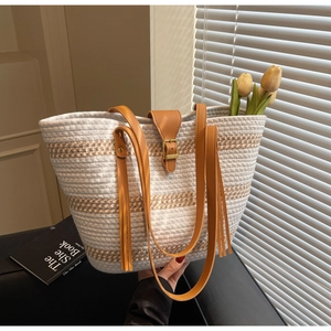 Detail of hand-woven straw tote with brown leather strap, fringe tassels and leather buckle