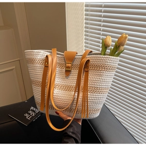 Detail of white woven straw tote bag with brown leather handles and buckle closure