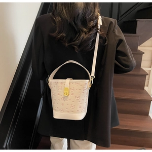 Detail of cream white bucket bag with bear embossing and gold lock shown worn crossbody