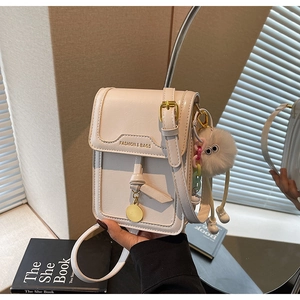 Close-up of cream square bag with gold buckle, plush charm, and leather texture