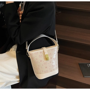 Detail view of beige bucket bag with pink bear print and gold clasp on wooden background