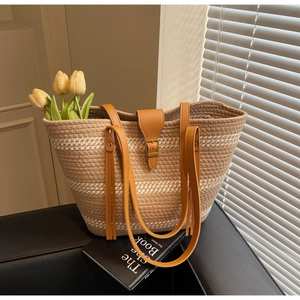Detailed view of woven straw tote bag with brown leather straps and elegant tassels