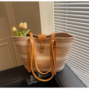 Detail of woven straw tote bag with brown faux leather straps and orange tassel accent