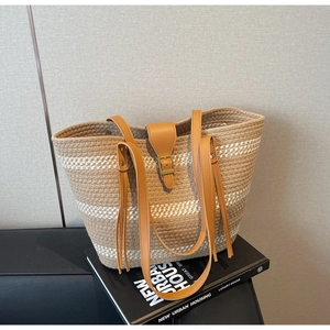 Detail of woven straw tote bag with brown leather straps and elegant fringe tassels