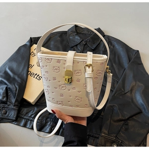 Close-up of beige bucket bag featuring bear embossing and gold twist-lock closure