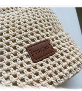 Détail de la texture tricotée du sac beige avec étiquette de marque en cuir brun