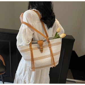 Detail view of woven tote bag with stripe pattern, brown leather handles and fringe tassel