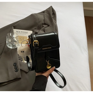 Detail of black faux leather phone bag with gold buckle strap and plush monster charm