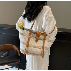 Detail of hand-woven straw tote bag with leather straps and long decorative fringe