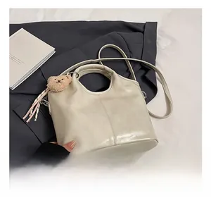 Detail view of beige bucket bag featuring sleek cutout handle and plush bear charm