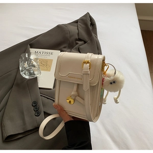 Detail of cream mini crossbody bag with leather texture and cute plush monster charm