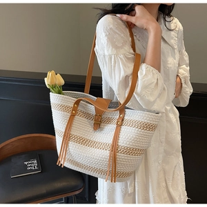 Detail of striped straw tote bag featuring leather handles and decorative long tassels