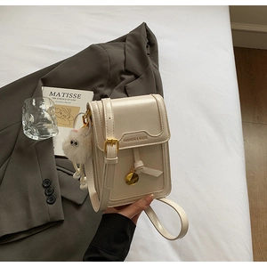 Detail of cream leather square crossbody bag with gold nameplate and fluffy charm