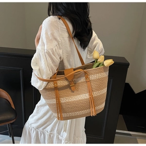Detail of hand-woven straw tote bag with brown faux leather straps and fringe accents
