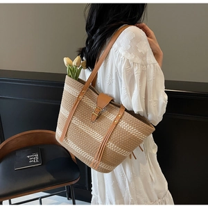 Detail of hand-woven straw tote bag with brown leather straps and metal buckle closure