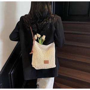 Détail du sac seau en maille ajourée avec bandoulière marron, perle rouge et logo en cuir