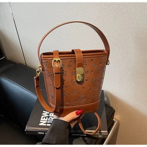 Detail showing brown bucket bag with embossed cartoon bears and gold lock hardware