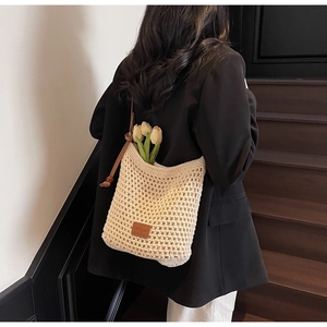 Vue détaillée du sac hobo en crochet beige ajouré avec écusson logo en cuir marron sur l'épaule