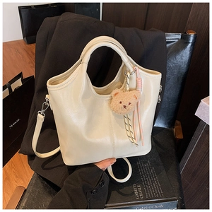 Detail of cream crossbody bucket bag with plush bear charm and striped rope accessory