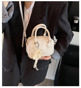 Dettaglio della piccola borsa bowling crema con ciondolo di perle e logo stampato