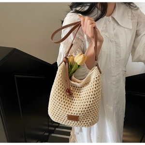 Détail du sac seau tissé beige avec bandoulière en cuir marron et écusson logo