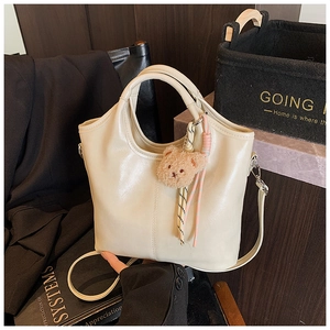 Detail of cream bucket bag with round handle, plush bear charm, and soft leather texture