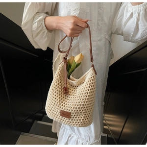 Détail du sac seau tissé crème avec logo en cuir marron et accents de perles en bois