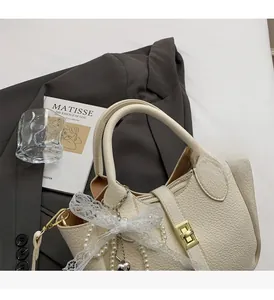 Detail of cream white lychee leather bucket bag with gold lock and lace bow charm