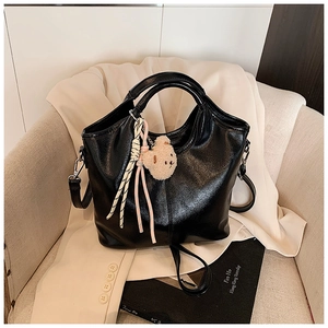 Detail of black glossy bucket bag with plush bear charm and woven tassel accessories