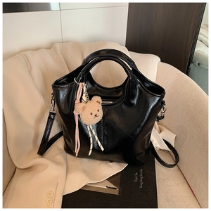 Detail of glossy black leather tote bag with cute teddy bear charm and braided strap