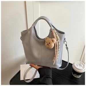 Close-up of light grey PU bucket bag with cute plush bear and colorful knotted rope details