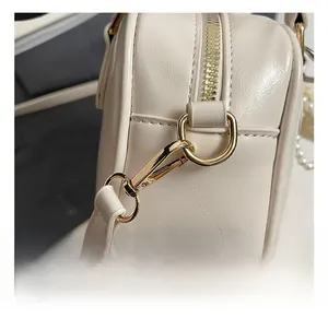 Dettaglio ravvicinato dei ganci in metallo dorato e anelli a D sulla borsa beige in pelle