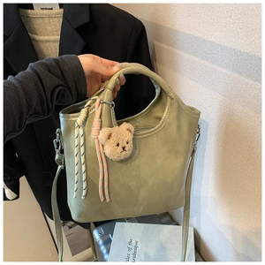 Detail of light green PU bucket bag with cute bear charm and woven straps on shoulder