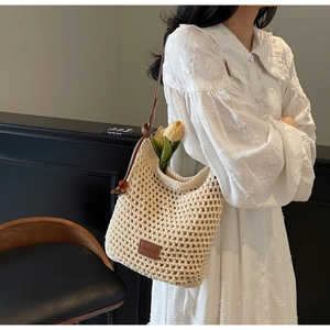Gros plan du sac seau en maille beige avec bandoulière en cuir brun et logo de marque