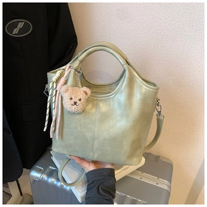 Detail of sage green bucket bag with vertical stitching and plush bear charm accent